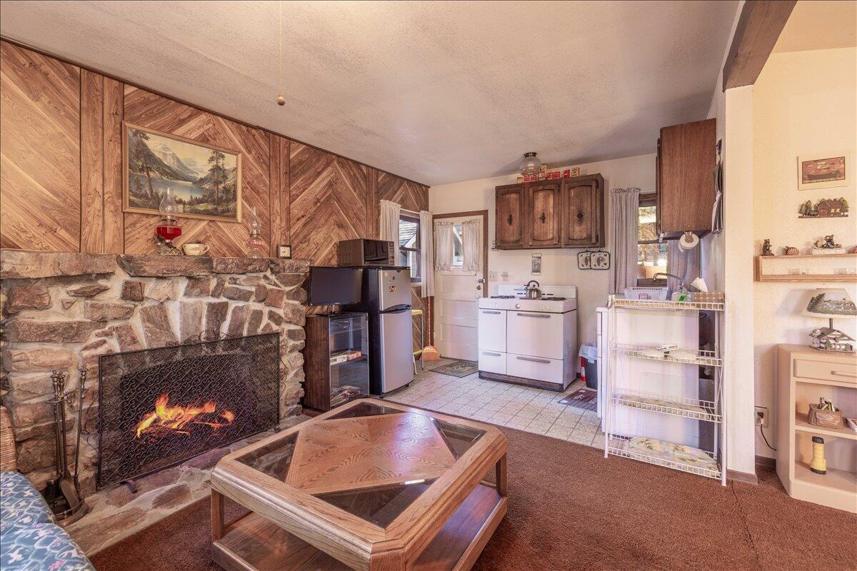 Living room with a native rock fireplace lit, wood plank walls, and an open floorplan into the kitchen